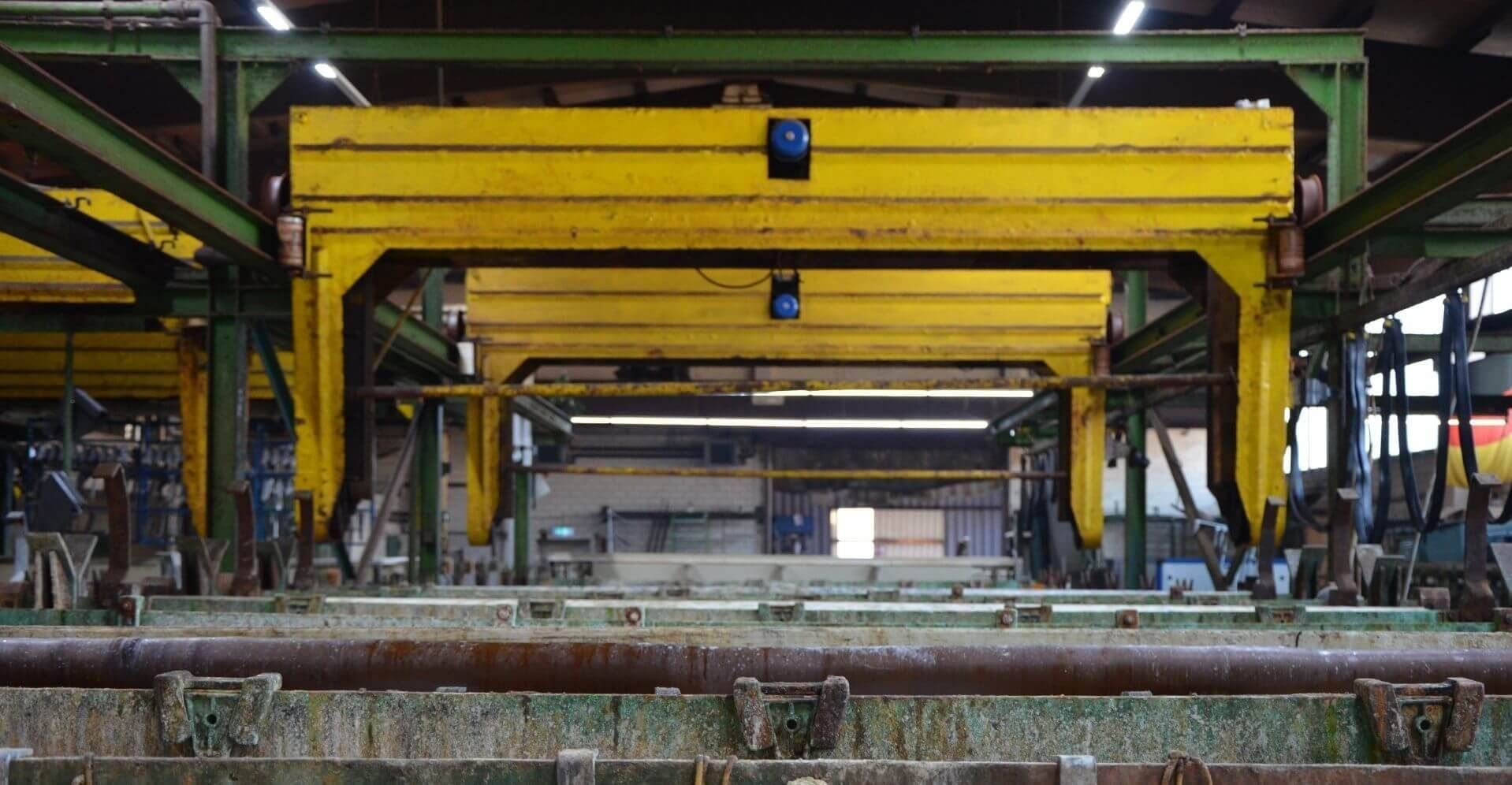 Das Innere einer Fabrik mit gelben Brückenkränen, grünen Strukturen und verrosteten Maschinen, die ein industrielles Umfeld darstellen